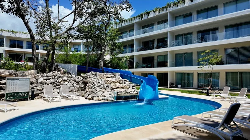 una alberca con un tobogan y camastros alrededor en the leaf condos playacar